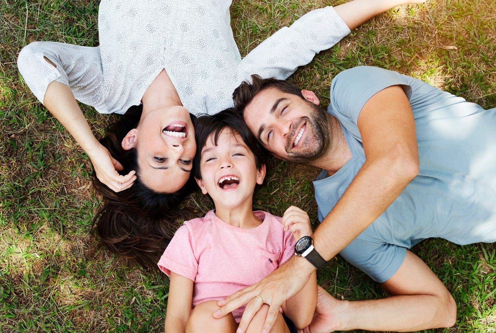 Mom, dad and a kid smiling on a grass field